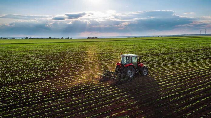 436506028 featured image Tractor plowing a vast green field at sunset.