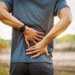 Person holding lower back in discomfort outdoors