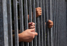 Hands gripping metal bars of a fence
