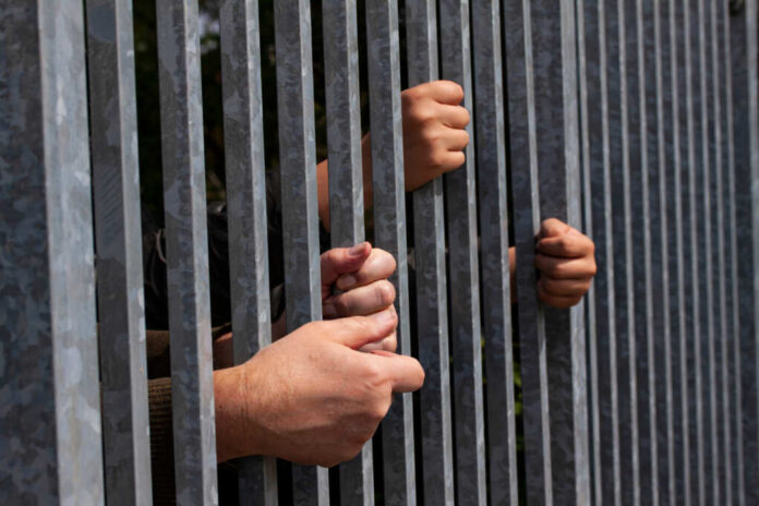 Hands gripping metal bars of a fence