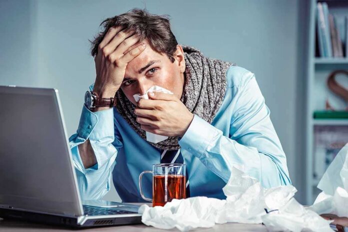 1112983769 featured image Man with tissue feeling unwell at laptop desk
