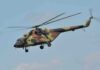 Camouflage military helicopter in flight against blue sky