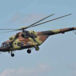 Camouflage military helicopter in flight against blue sky