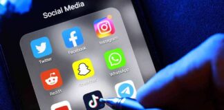 Social media apps on phone screen with hand holding stylus