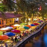 Outdoor riverside restaurant with colorful umbrellas and evening lights.