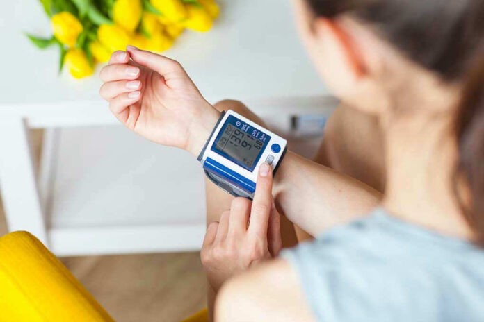 Person checking wrist blood pressure monitor indoors