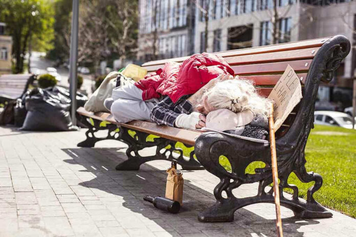 Person sleeping on park bench with cardboard sign.