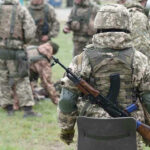 Soldiers in camouflage gear gathered on grass field.