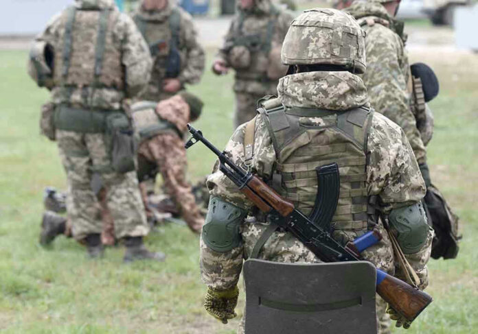 Soldiers in camouflage gear gathered on grass field.