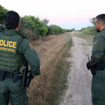 Armed Cartels Invade Protected U.S. Parkland Two U.S. Border Patrol officers observing a dirt path.