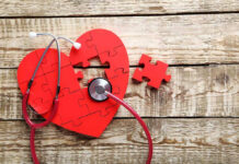 Red heart puzzle with stethoscope on wooden background