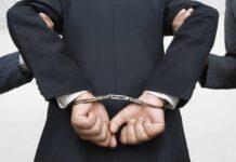 A person in a suit with hands cuffed behind their back
