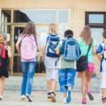 Student Spying Exposed – Not Just in Class! Group of children walking towards a school entrance with backpacks