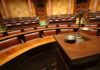 A courtroom with empty seats and a scale of justice in the foreground
