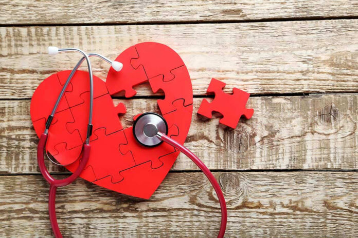 Red heart puzzle with stethoscope on wooden background