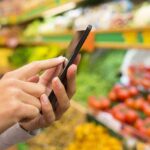 Person using a smartphone while shopping for fresh produce in a grocery store