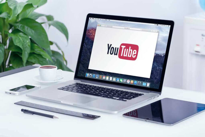 Laptop displaying YouTube with coffee and stationery nearby.