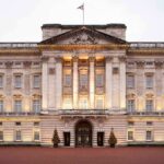 Giuffre Memoir Stuns Royals Front view of Buckingham Palace with illuminated facade and British flag