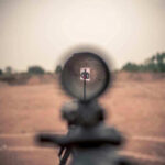 U.S. Citizens Target Haiti — Heinous Genocide Plot Rifle scope aimed at a distant target outdoors.
