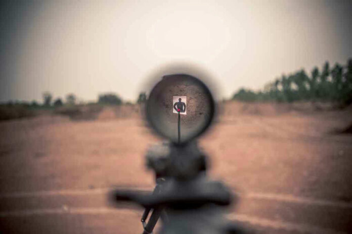 Rifle scope aimed at a distant target outdoors.