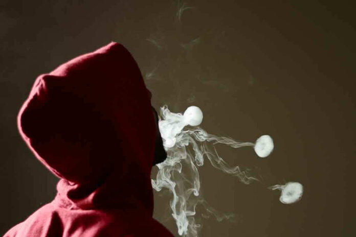 Person in red hoodie blowing smoke rings.