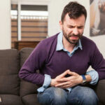 Surprise Virus Shift: Norovirus Alters Seasonal Norms Man sitting on couch, holding stomach in pain.