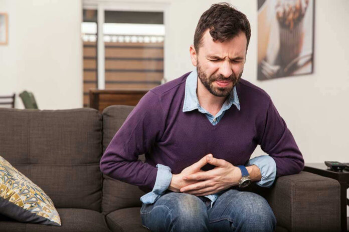 Man sitting on couch, holding stomach in pain.