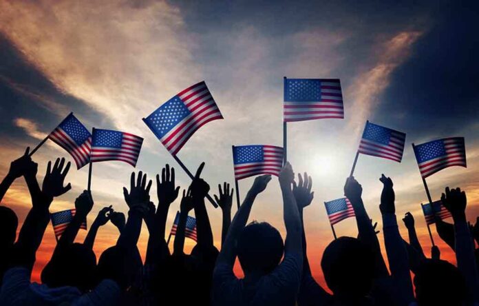 Silhouetted crowd holding American flags against a sunset sky
