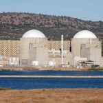Nuclear power plant with domed structures beside a water body and mountains in the background