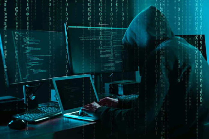 Hacker in dark room surrounded by computer screens.