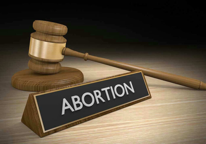 Gavel and sign reading Abortion on a wooden surface.