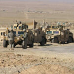 Soldiers beside military vehicles in a desert area.