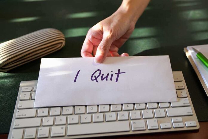 shutterstock_1338161933.jpg A hand placing an envelope labeled 'I Quit' on a keyboard