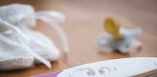 A pregnancy test next to a pacifier and a knitted baby hat on a wooden surface