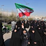 Group of women in black attire marching with an Iranian flag