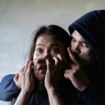 Man holding womans mouth, gesturing silence.