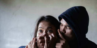 Man holding womans mouth, gesturing silence.