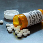 Opioid Misunderstanding Hurts Millions Open pill bottle with white tablets spilled out.