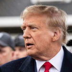 Man in suit and red tie speaking outside.