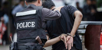 Police officer arrests handcuffed person.