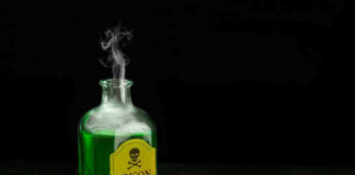 Green poison bottle with cork on wooden surface.