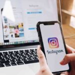 Parents ALERTED: Teen’s Dangerous Searches! Person holding a smartphone displaying the Instagram logo with a laptop in the background