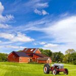 A vintage tractor in front of a red barn on a sunny day