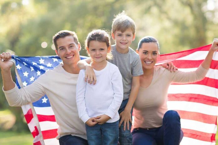 A family of four posing outdoors with an American flag