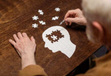 Elderly person completing head-shaped jigsaw puzzle.