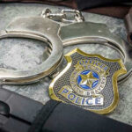Badge Abuse Shock: Ex-Cop Indicted Handcuffs, officer badge, and firearm on textured surface.