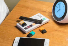 Vape pen, smartphone, clock on wooden table.