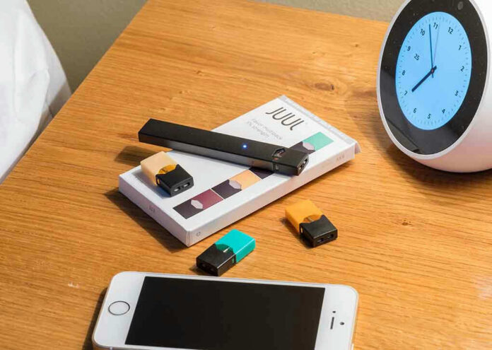 1164563215 Vape pen, smartphone, clock on wooden table.