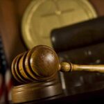 A wooden gavel resting on a desk in a courtroom with an American flag in the background