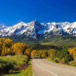 Scenic view of snow-capped mountains with autumn trees and a winding road